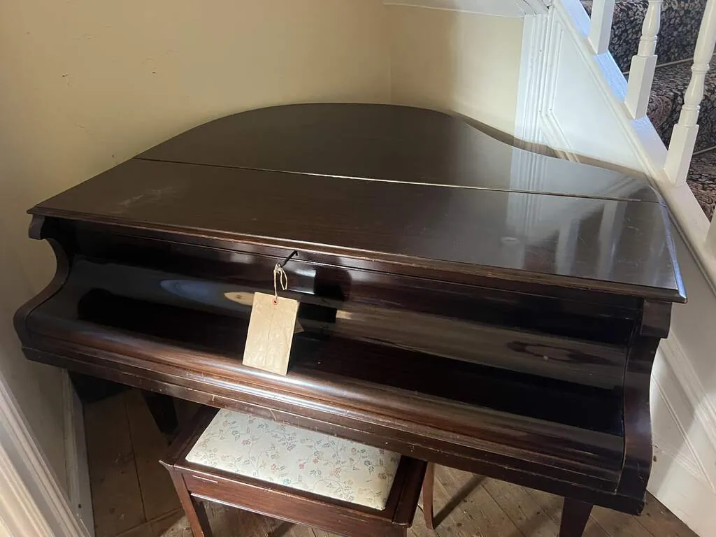 Mahogany Amyl baby grand piano in a corner beside a staircase in north Sheffield, with its original maker's tag hanging from the key in the lock