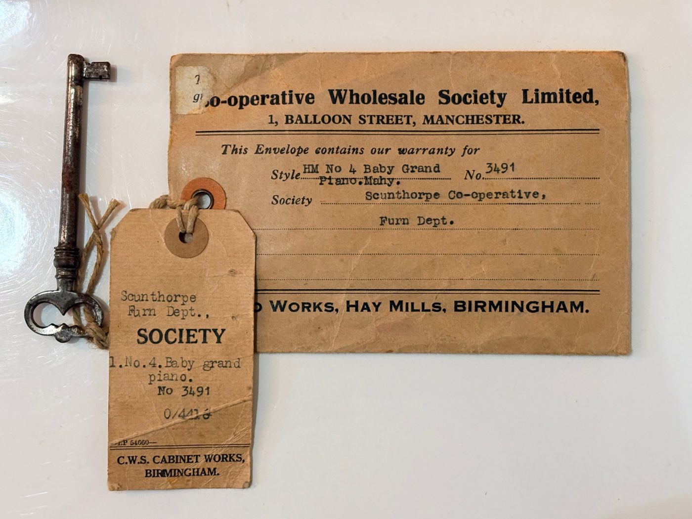 Original key on its string, C.W.S. Cabinet Works maker's tag for a No. 4 baby grand piano number 3491, and the Co-operative Wholesale Society warranty envelope