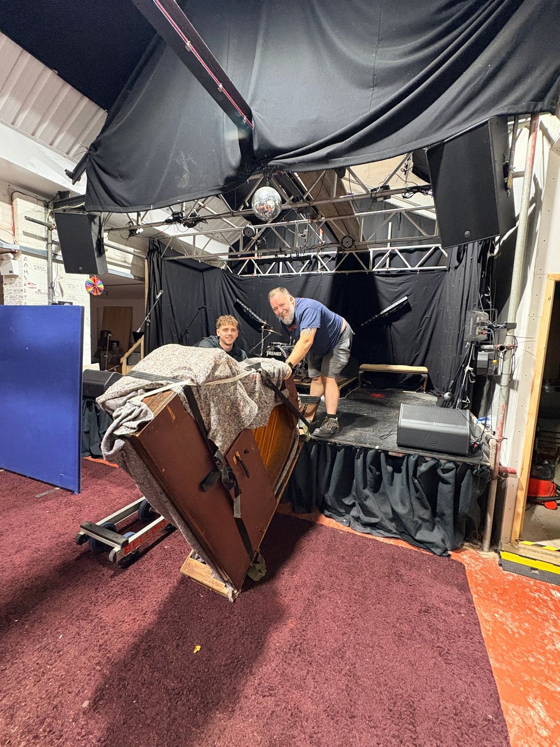 Wrapped grand piano in its skid being brought down from the stage to the floor onto a piano dolly at Mary St Live, Sheffield