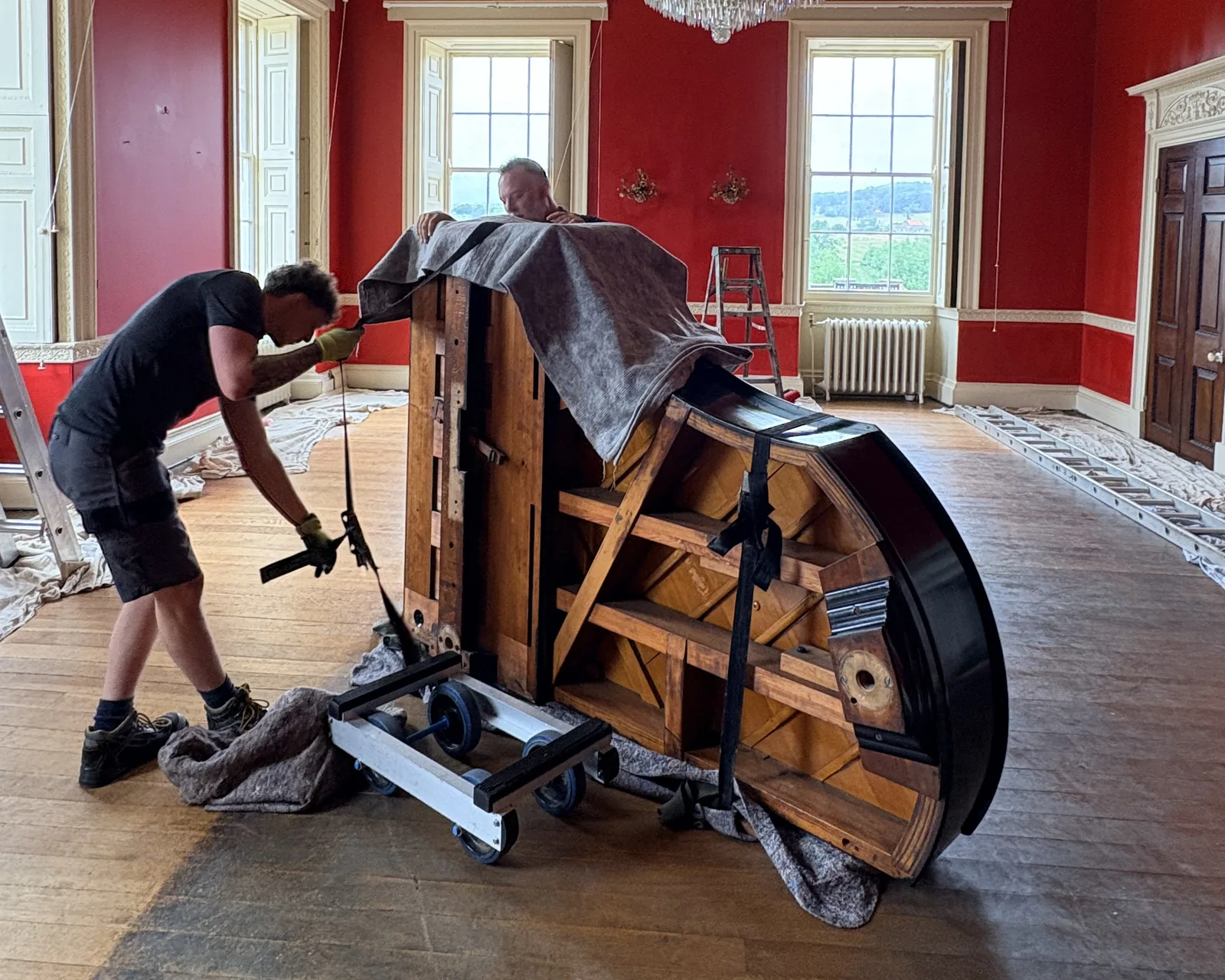 Two piano movers strapping a grand piano onto a piano board ready for removal