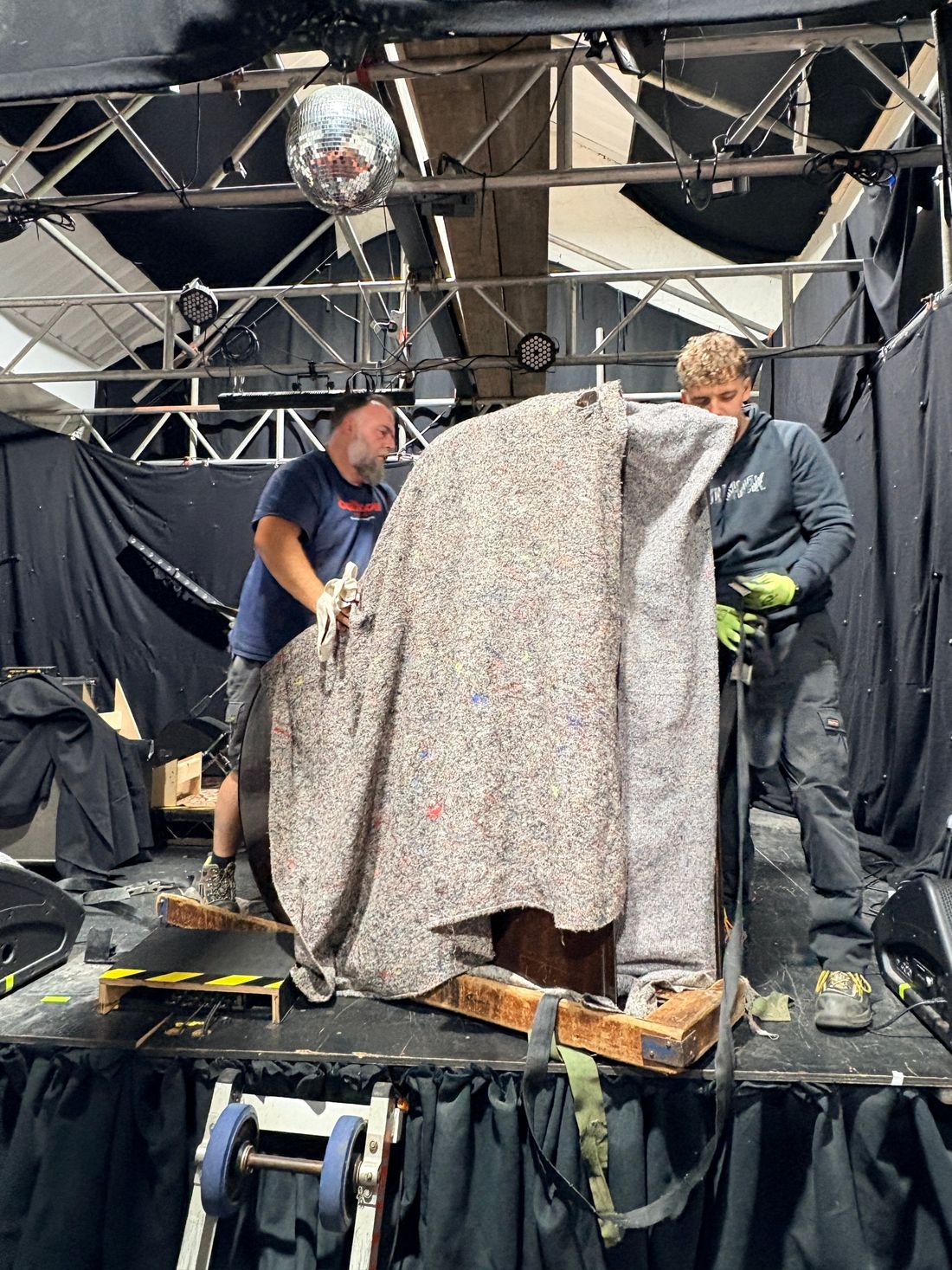 Yorkshire Piano Logistics movers wrapping a small grand piano in moving blankets in its skid, on the stage at Mary St Live in Sheffield