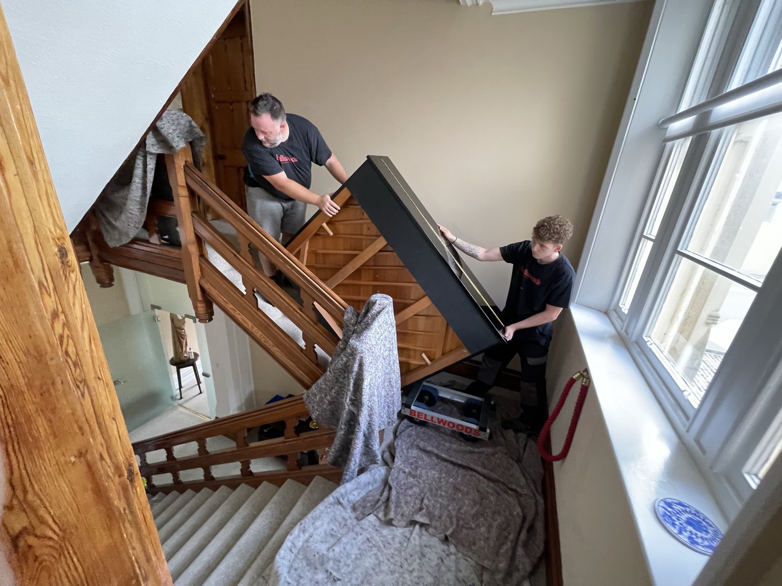 Piano being carried down a period staircase with banisters and treads padded, Harrogate