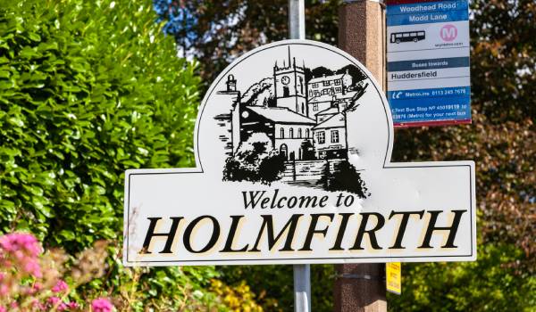 Welcome to Holmfirth sign beside a bus stop for Huddersfield
