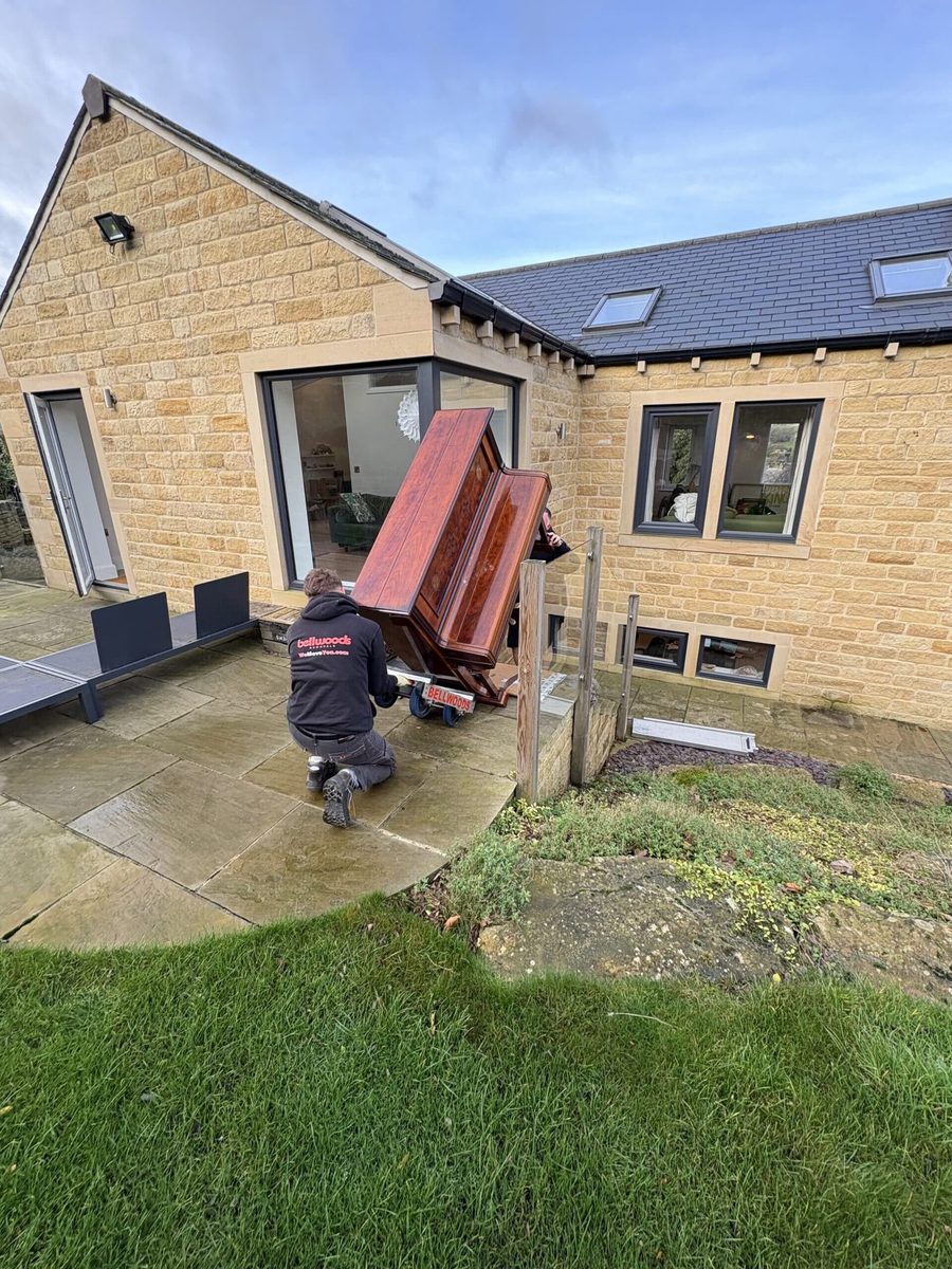 Upright piano being moved at a stone cottage in Holmfirth