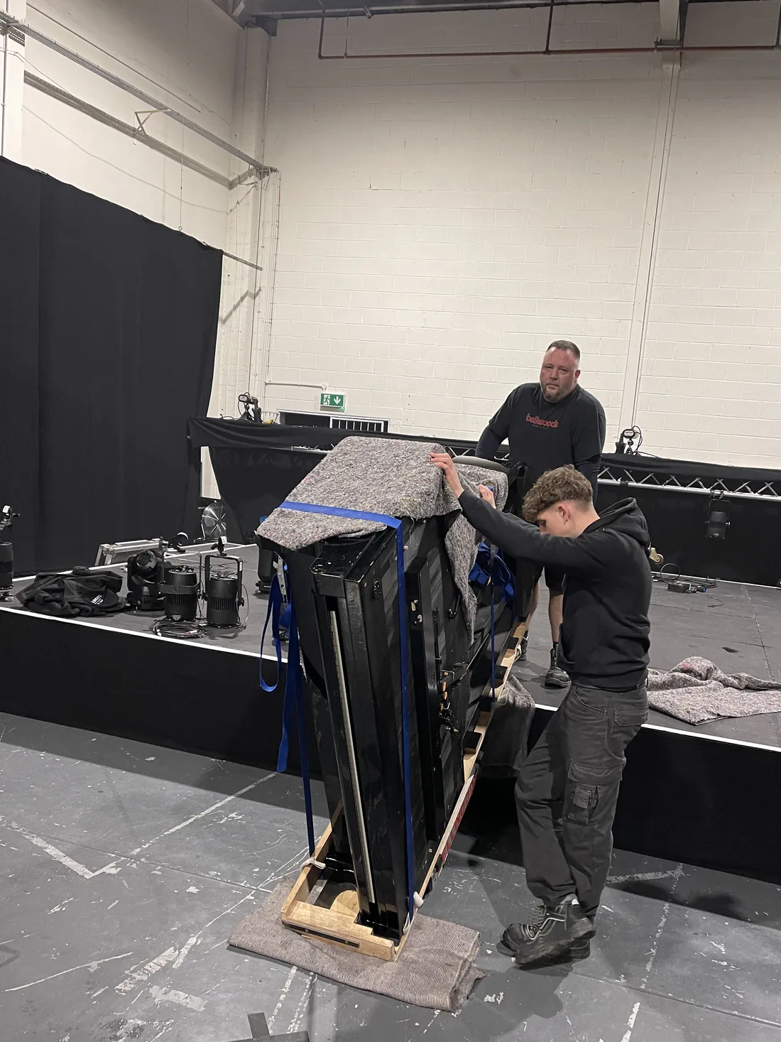 Piano strapped to a skid board and blanket-wrapped for a venue move